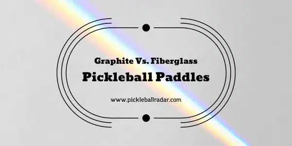 A promotional image with a double oval border featuring the text 'Graphite Vs. Fiberglass Pickleball Paddles' in the center and the URL 'www.pickleballradar.com' below it. The background is gray with a rainbow light flare crossing from the top left to bottom right.
